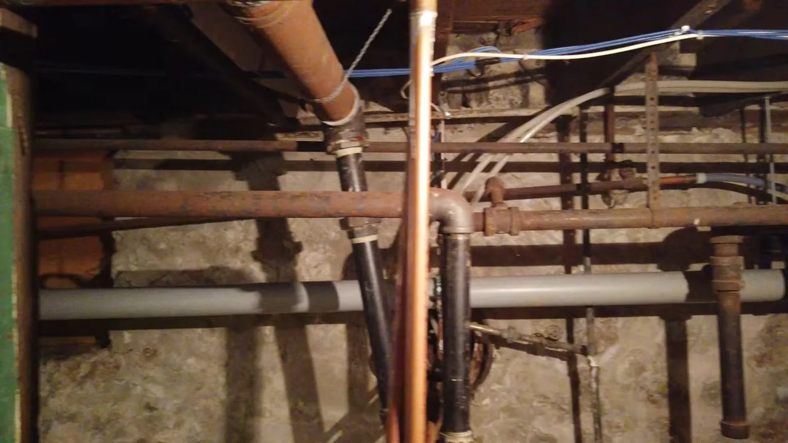 Basement ceiling with copper, cast iron and gray PVC pipes running side by side