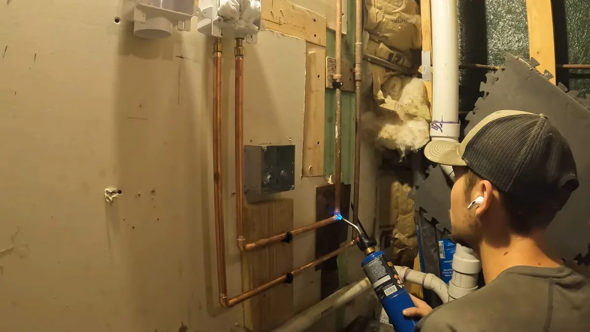 Man holding a torch to a copper joint inside an opened wall