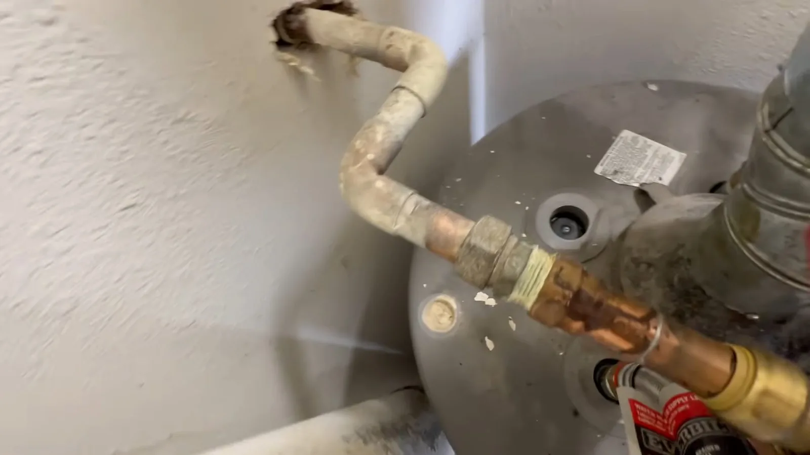 Copper and flexible pipes connecting to the top of a gray water heater beside a wall opening