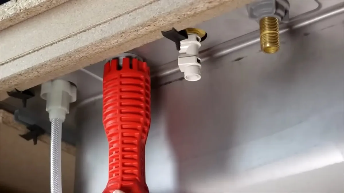 Red basin wrench reaching up to faucet fittings and a supply line under a sink