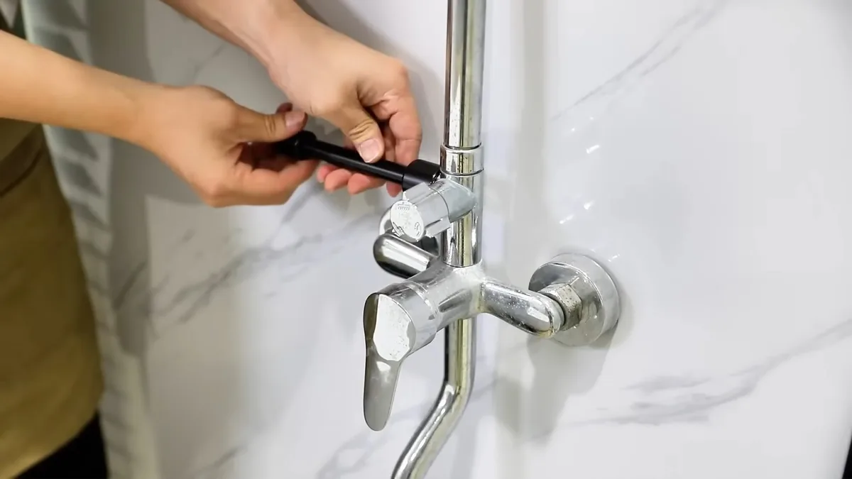 Hands tightening a small screw on a chrome shower arm against marble-look tile