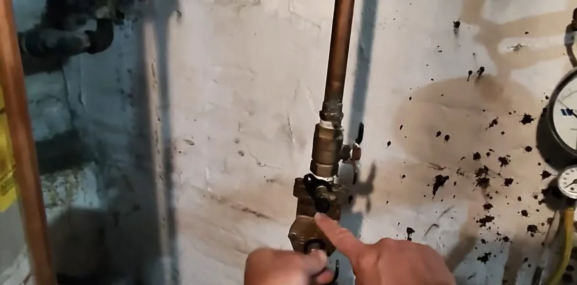 Finger pointing at a valve on a copper line against a wall with dark splatter