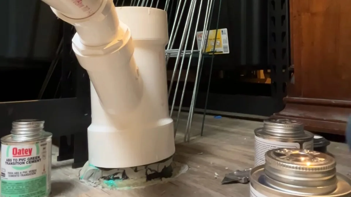 White PVC drain assembly rising from a floor beside cans of pipe cement and cleaner