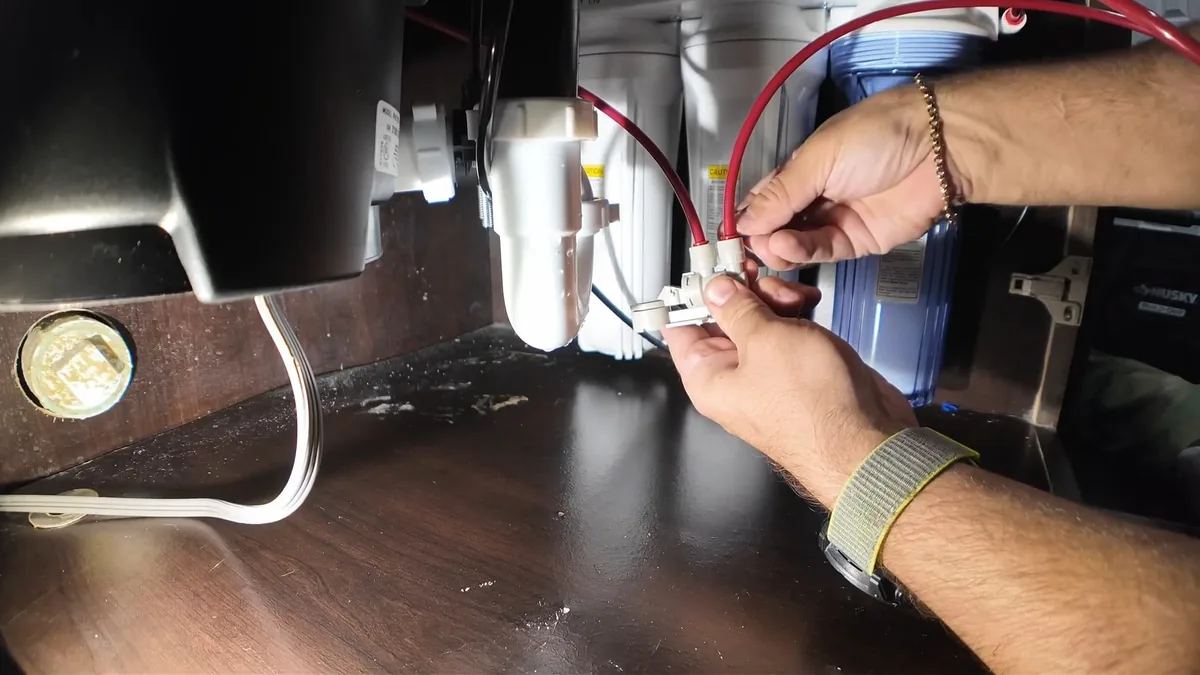 Hands joining white and red wires under a counter beside a black under-sink unit