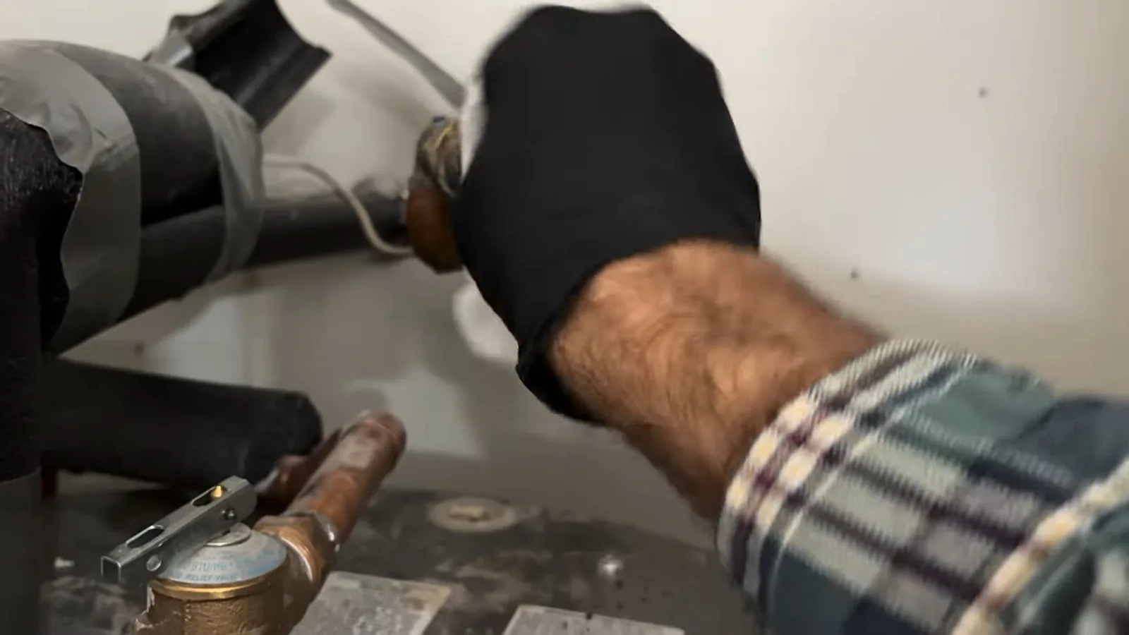 Gloved hand on insulated pipes and a valve above the top of a tank