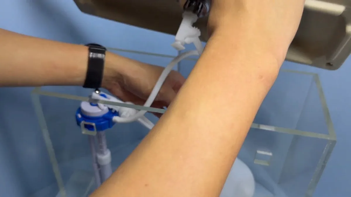 Hands adjusting a blue fill valve and float inside a clear toilet tank