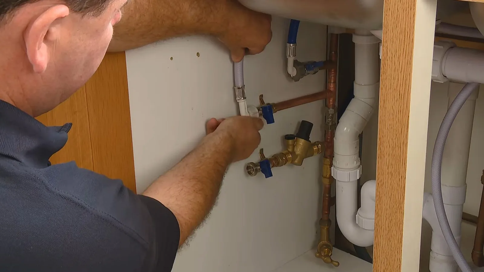 Man in a navy shirt reaching up under a vanity to work on supply lines and shutoff valves