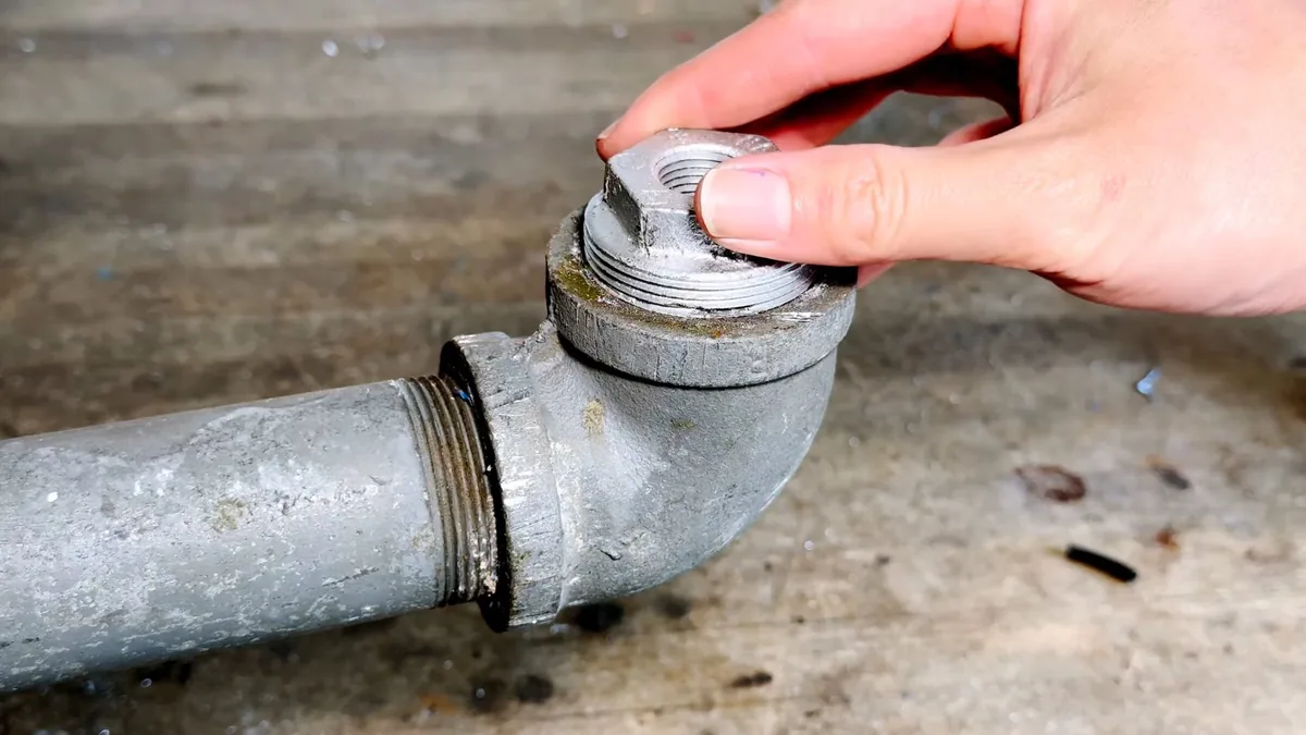 Hand unscrewing a threaded cap from a galvanized cleanout fitting at floor level