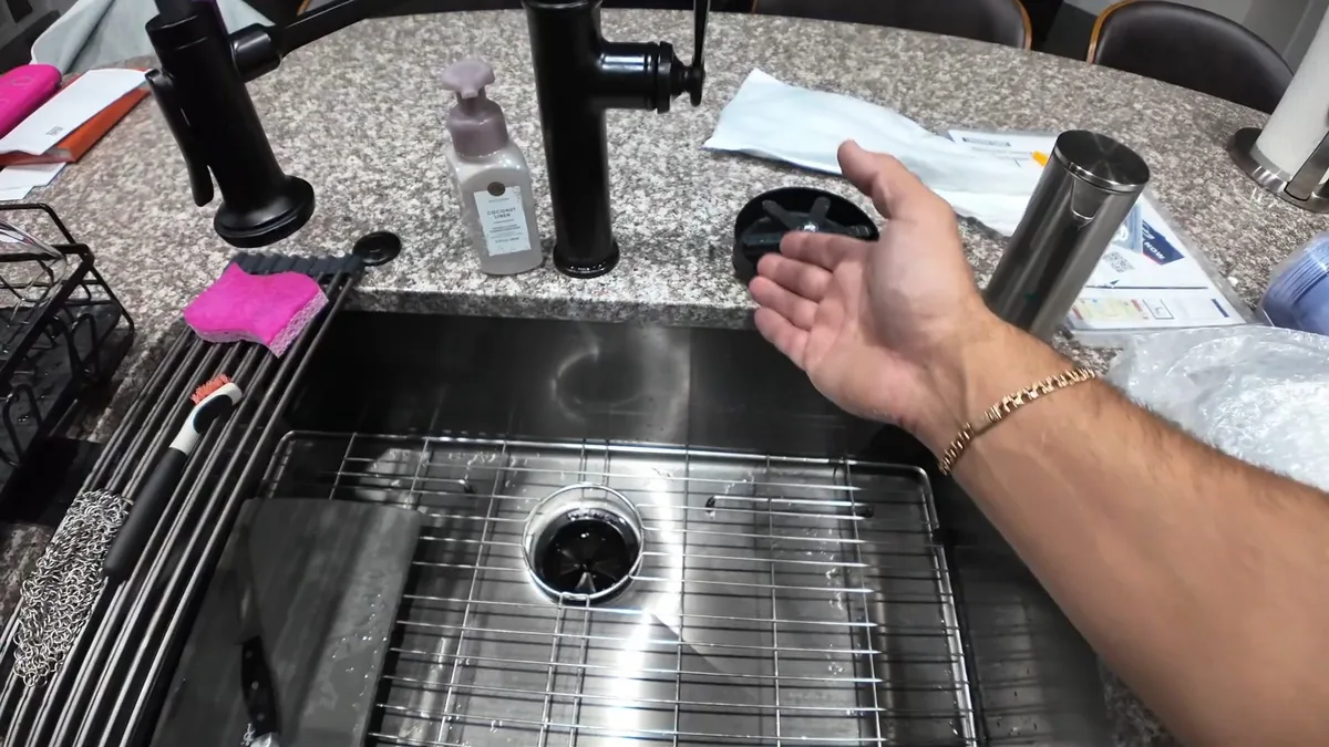 Hand held over a stainless sink with a black faucet and a drain grid