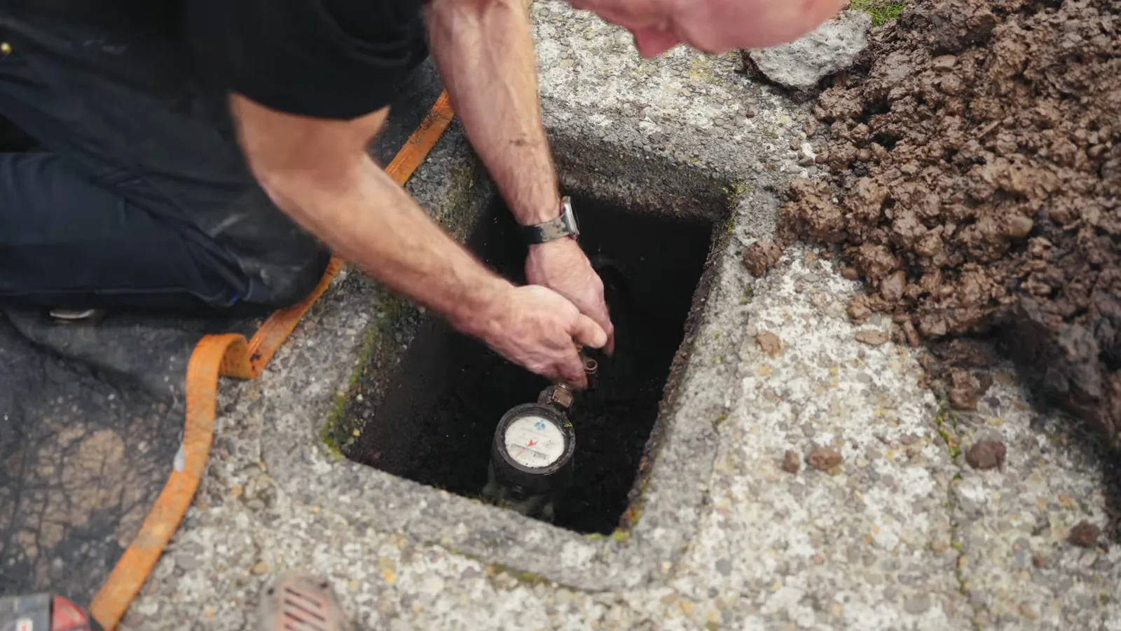 Technician's hands reaching into a concrete box to check a water meter dial