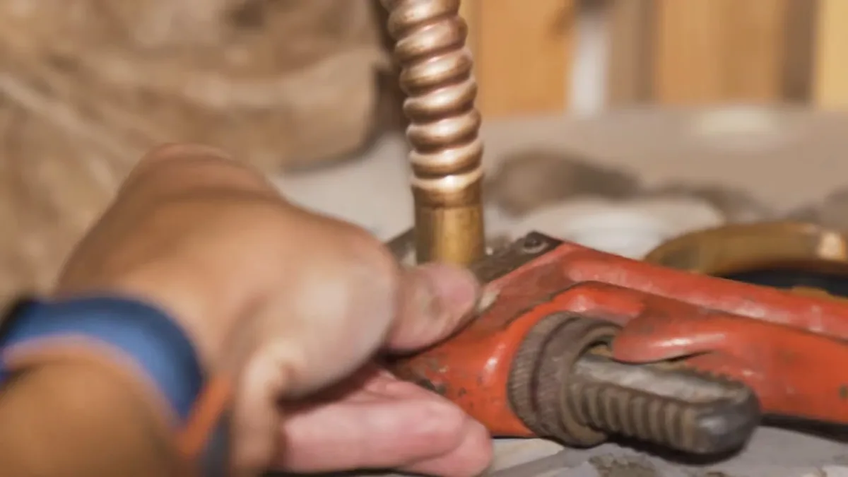 Hand holding a pipe wrench on a copper supply tube