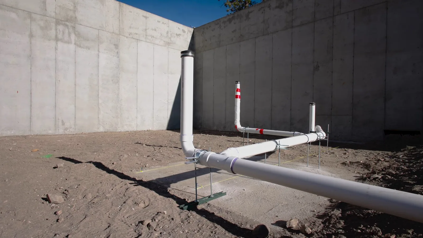 White PVC vent pipes standing on a bare dirt lot in front of concrete walls