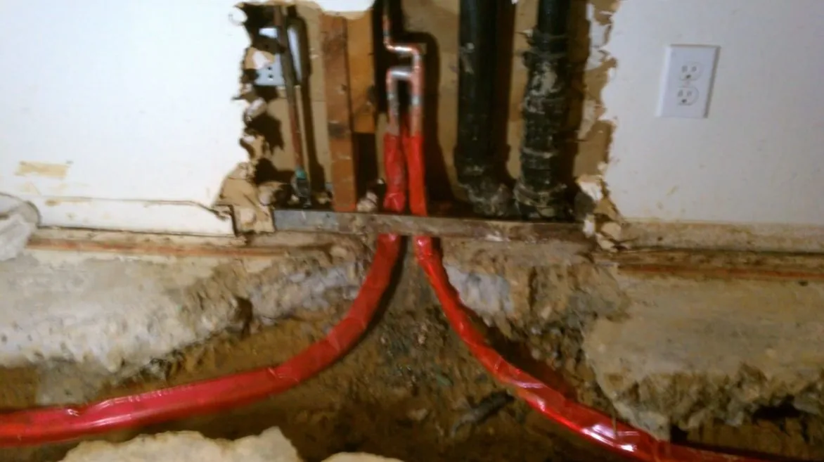 Opened wall at the floor line with red PEX lines running down through old framing