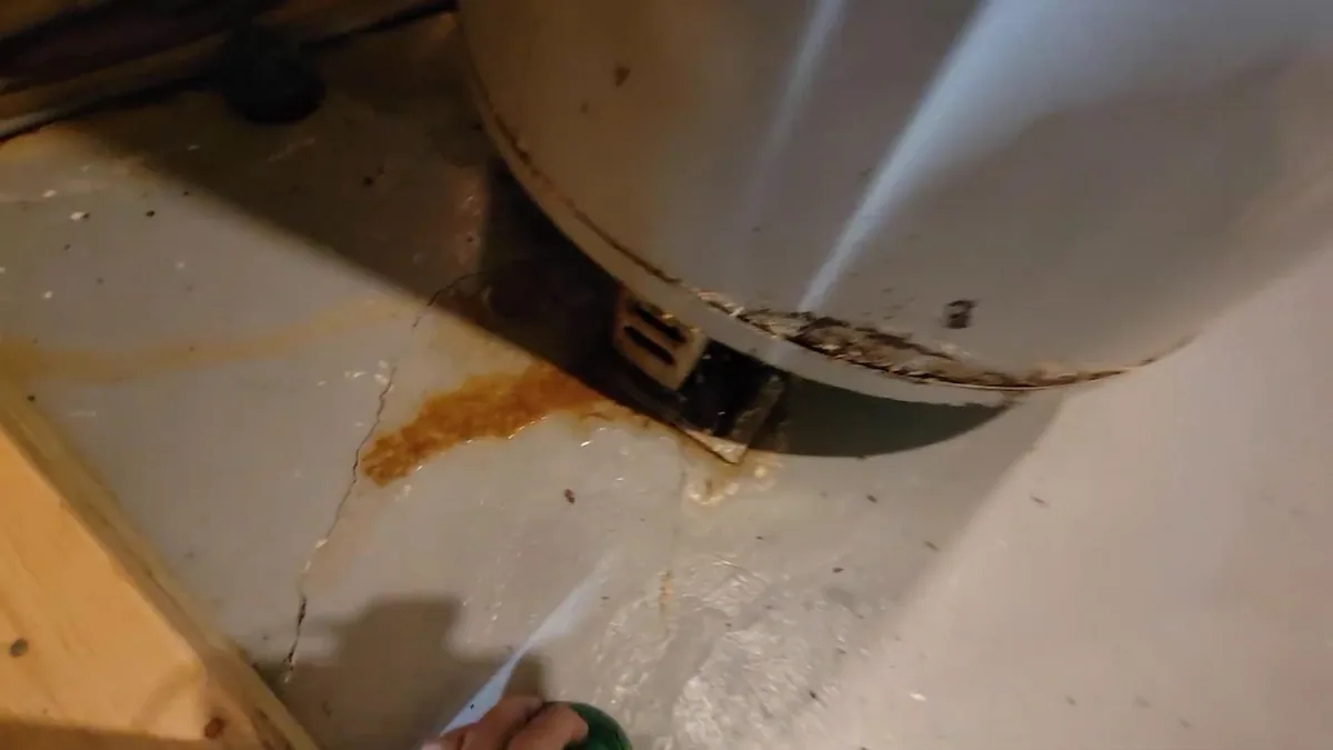 Rust stain and drip marks on the floor beneath the base of a water heater