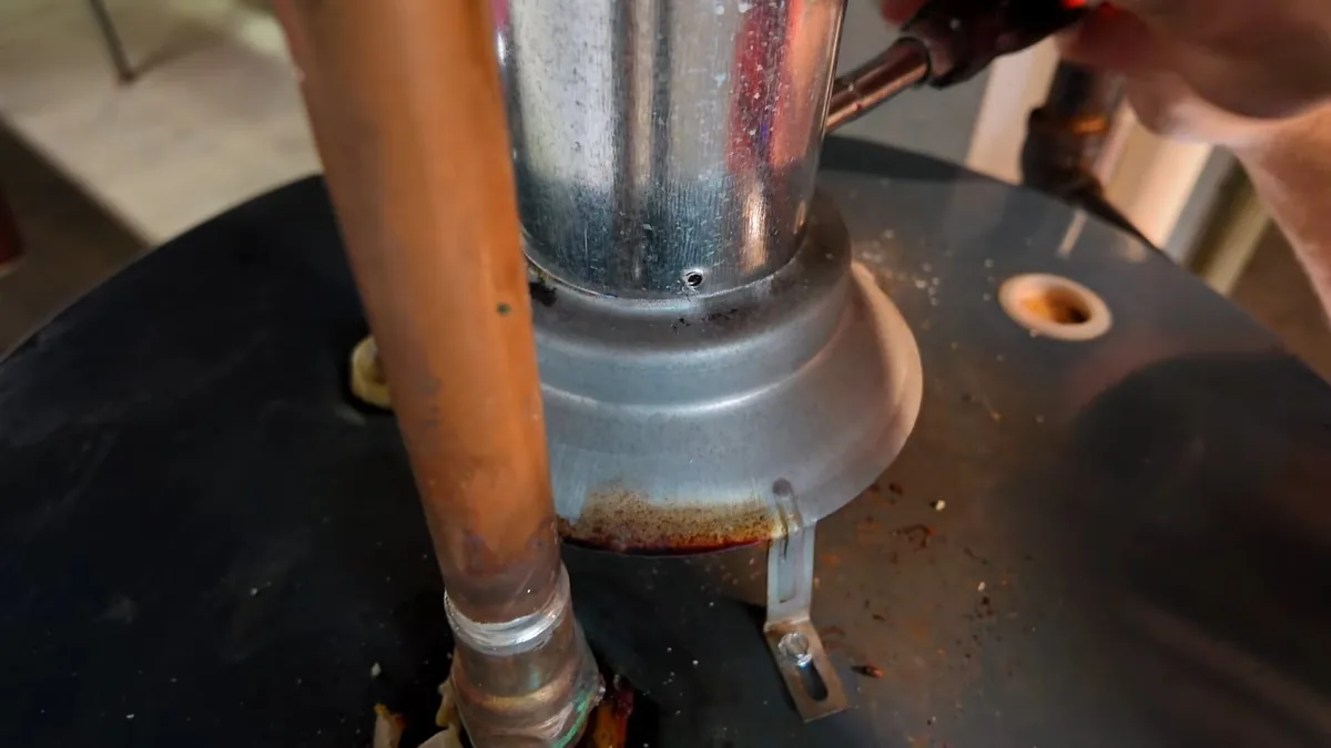 Rust-stained copper pipe and a metal flue collar on top of a black tank water heater