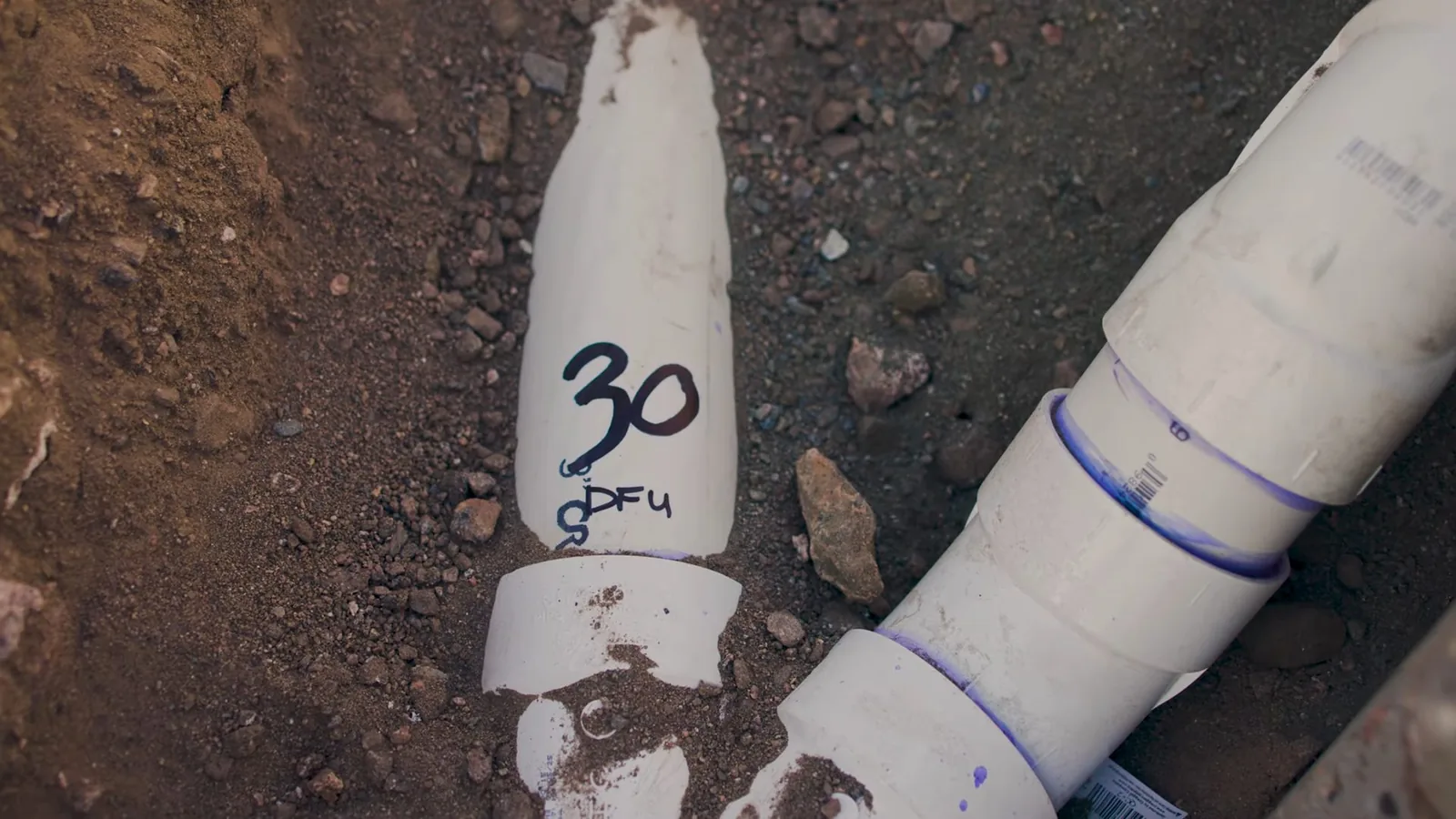 Large white PVC drain pipes joined in a dirt trench, one marked in black with a number