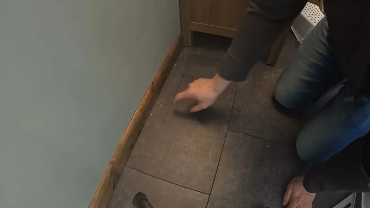 Hand pressed flat on a dark tile floor beside a baseboard