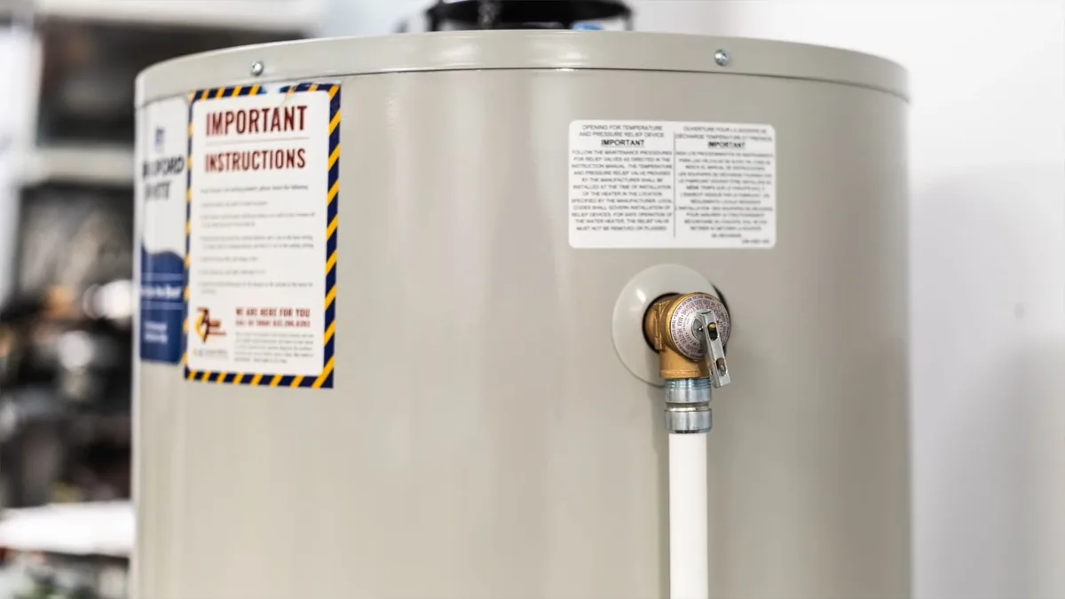 Close view of the side of a tank water heater with instruction labels and a hot water outlet