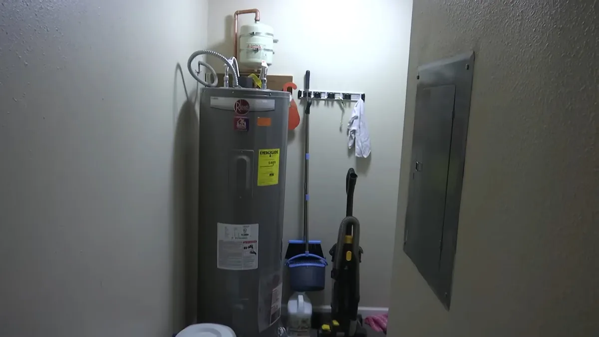Gray tank water heater in a utility closet next to an electrical panel, with the rating label facing out