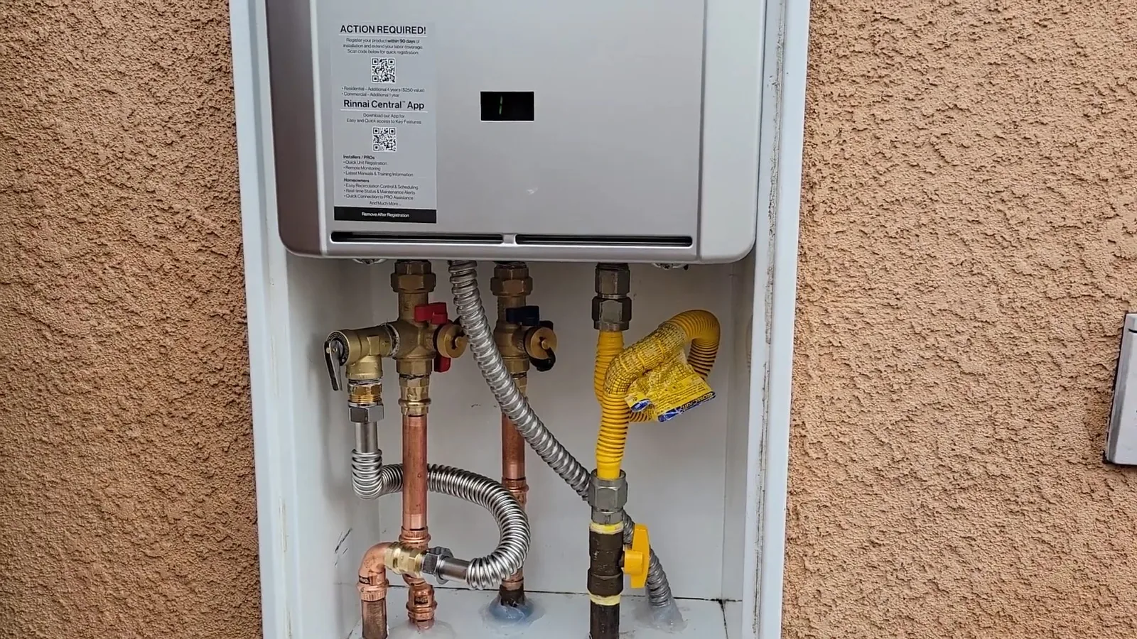 Wall-mounted tankless water heater in a recessed stucco niche with copper and yellow gas lines below