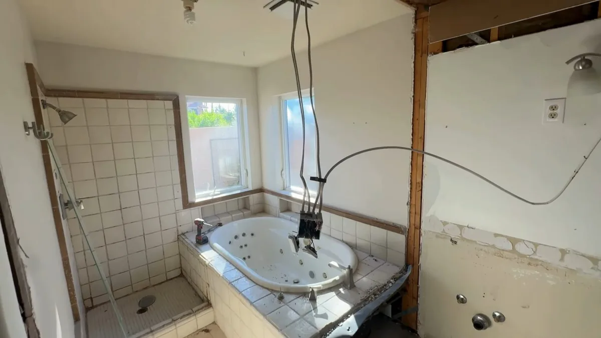 Bathroom with wall sections and flooring removed down to the studs around a tub