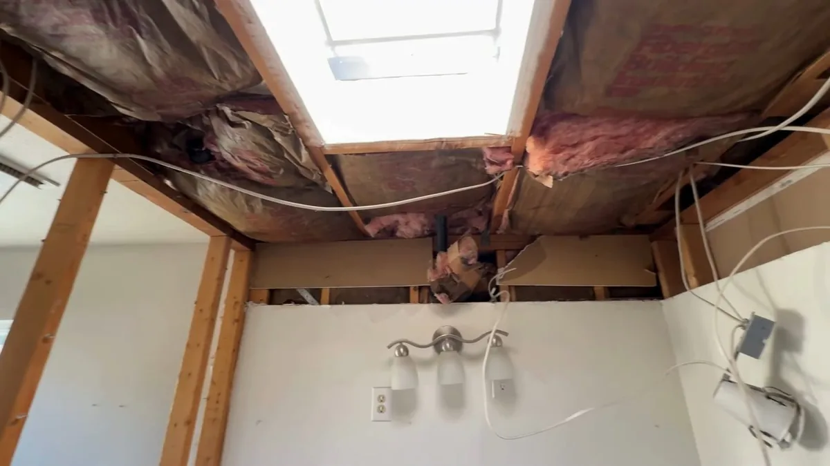 Ceiling opened between joists with pink insulation exposed above a light fixture and a skylight shaft