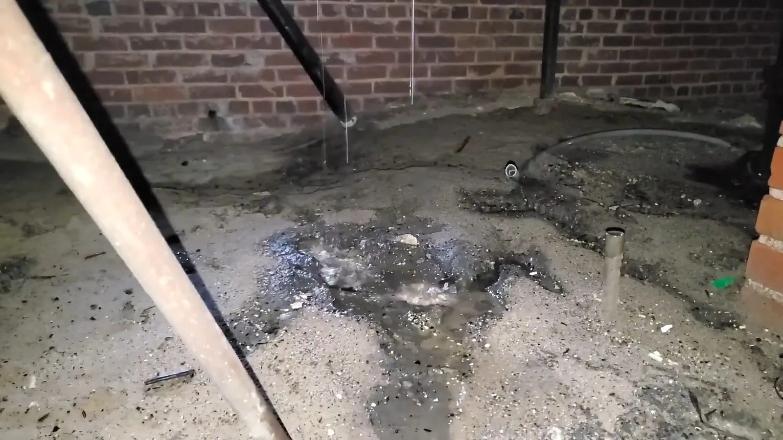 Wet gray mud and standing water across a crawlspace floor beside a brick wall