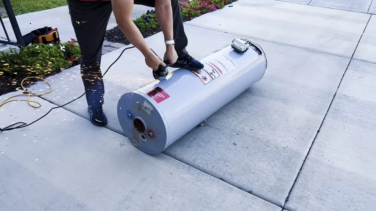Man tipping an old white tank water heater onto its side on a concrete driveway