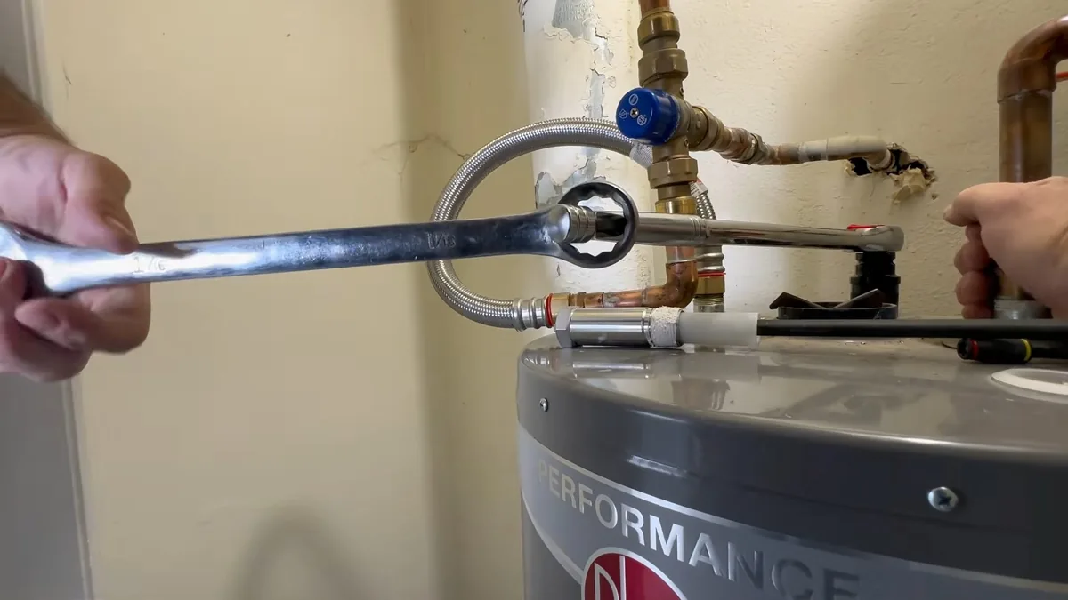 Wrench turning a nut on a braided flexible connector at the top of a gray water heater