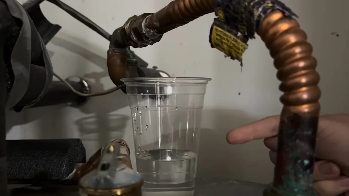 Clear cup held under a copper pipe on a water heater to catch dripping water