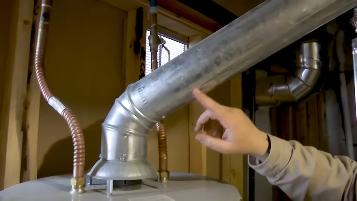 Hand pointing at a metal vent pipe rising from the top of a water heater