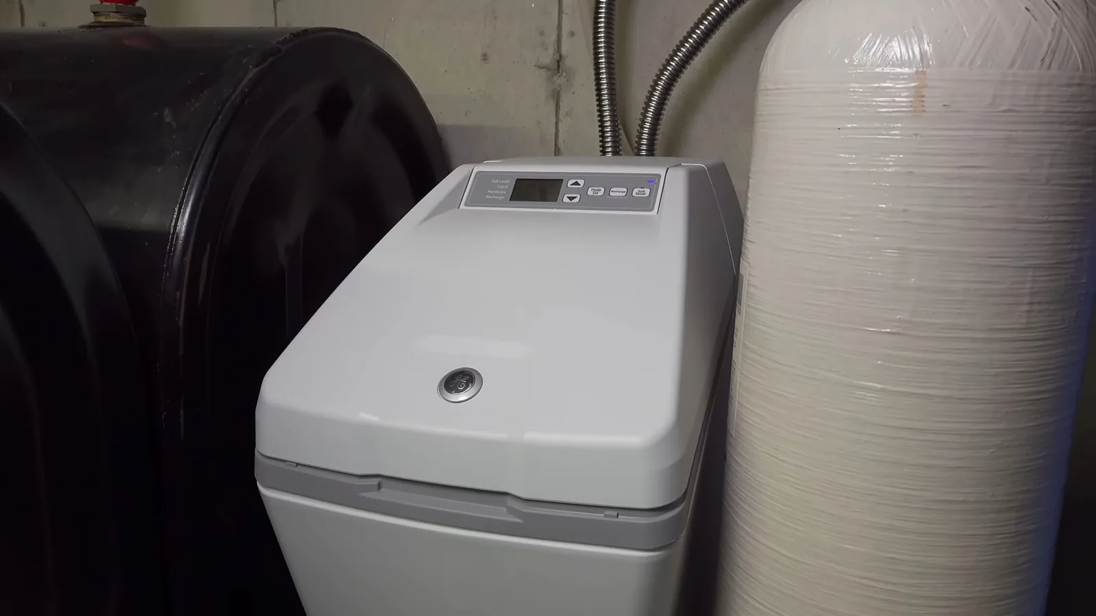 Gray water softener cabinet beside a black tank and a tall white tank in a basement corner
